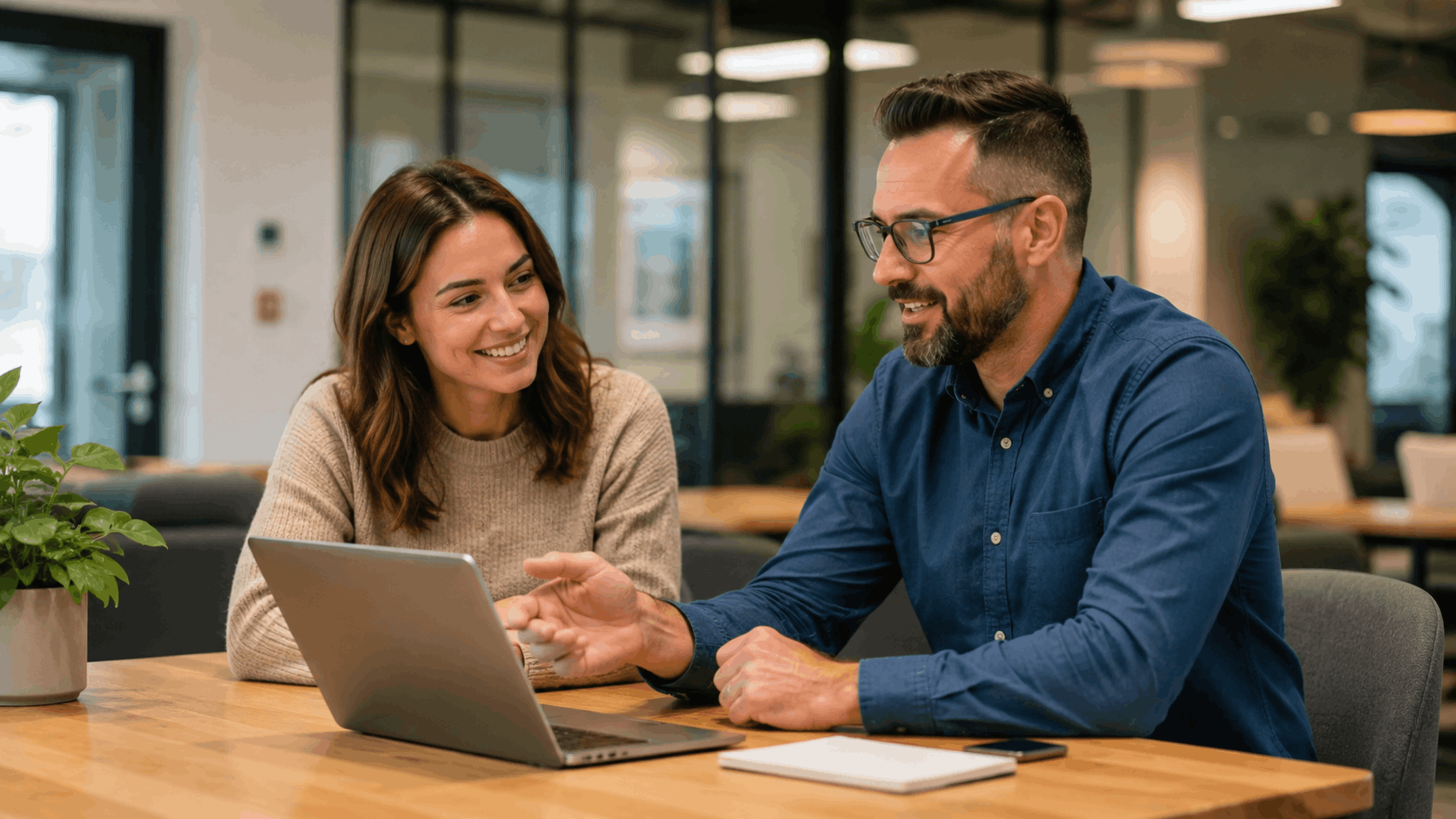 Two colleagues smiling while reviewing FAQ answers together on a laptop in office