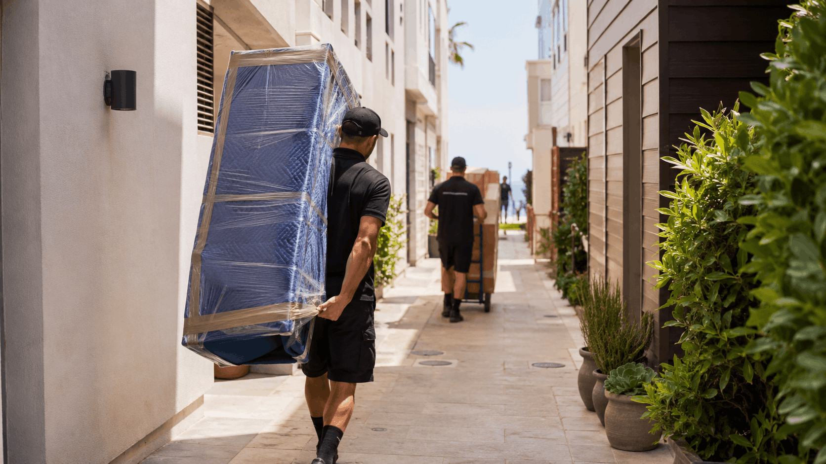 Two professional movers carrying mattress and boxes through narrow Los Angeles alleyway