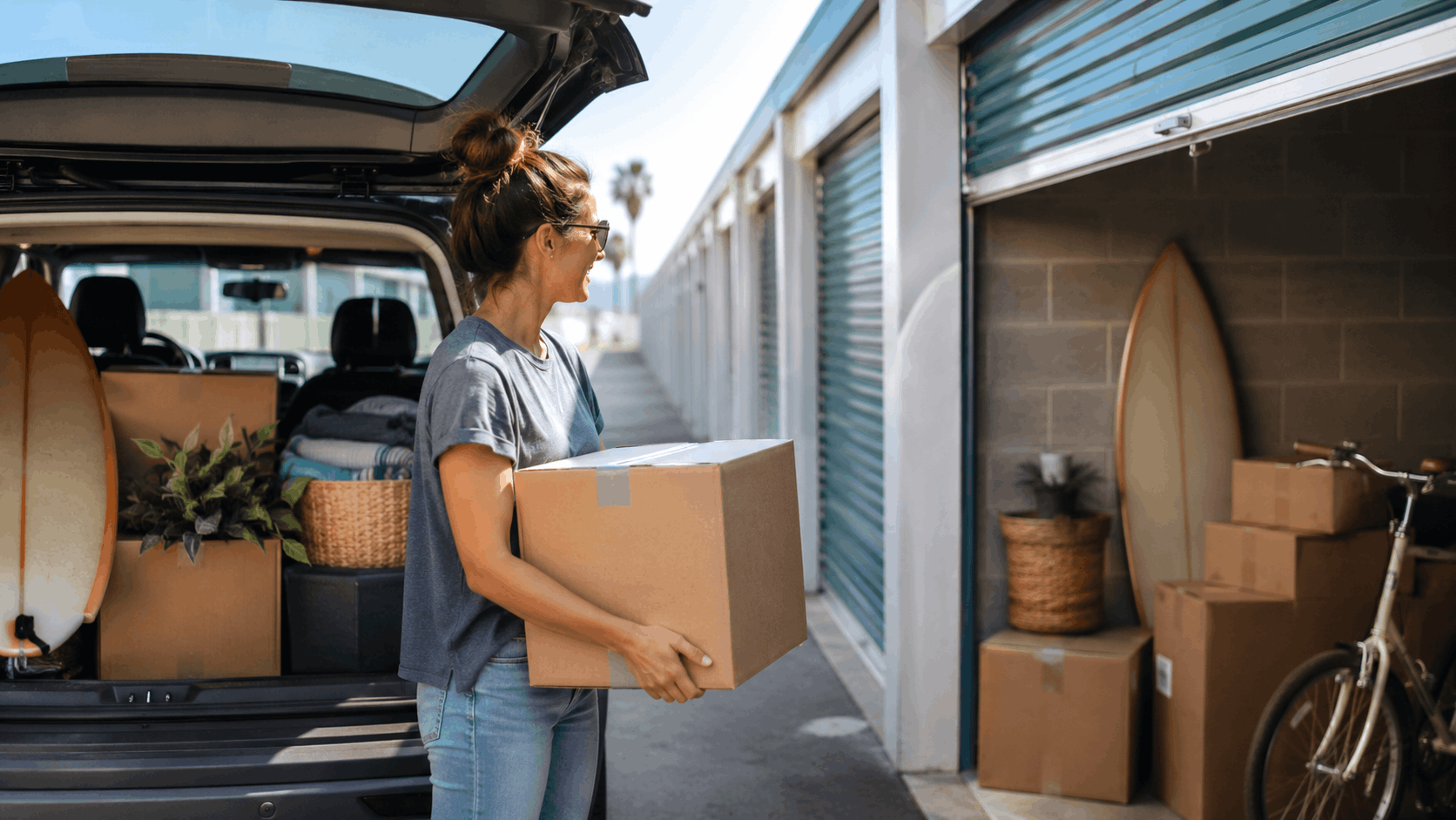Woman carrying cardboard box into open self-storage unit near Los Angeles coast
