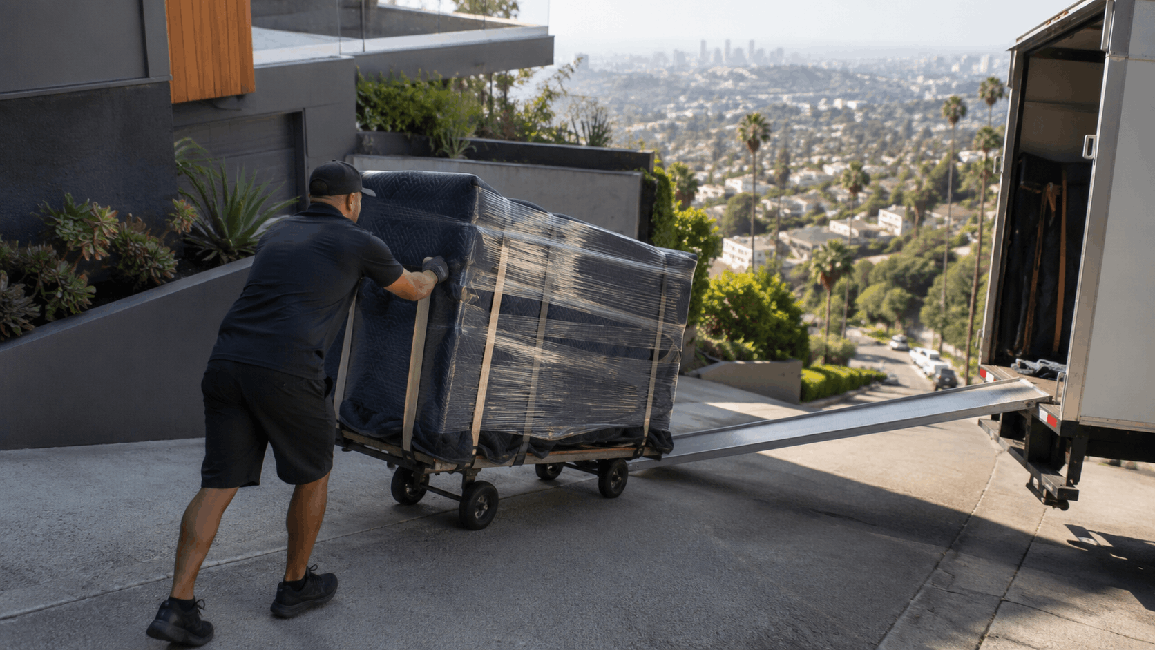 Popeye Moving worker pushing wrapped furniture up truck ramp at Los Angeles hillside home