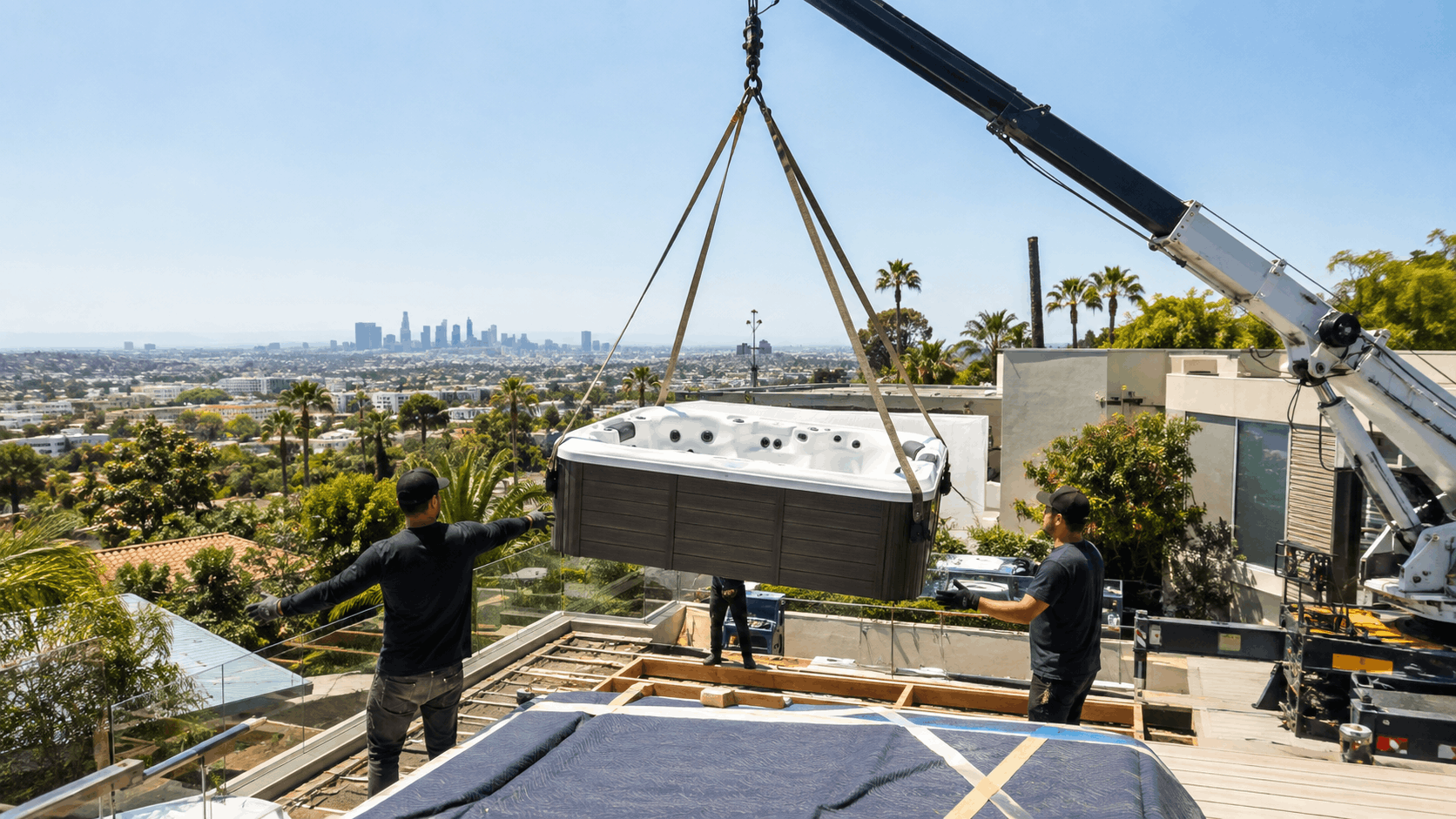 Crane lifting hot tub onto rooftop deck overlooking Los Angeles skyline