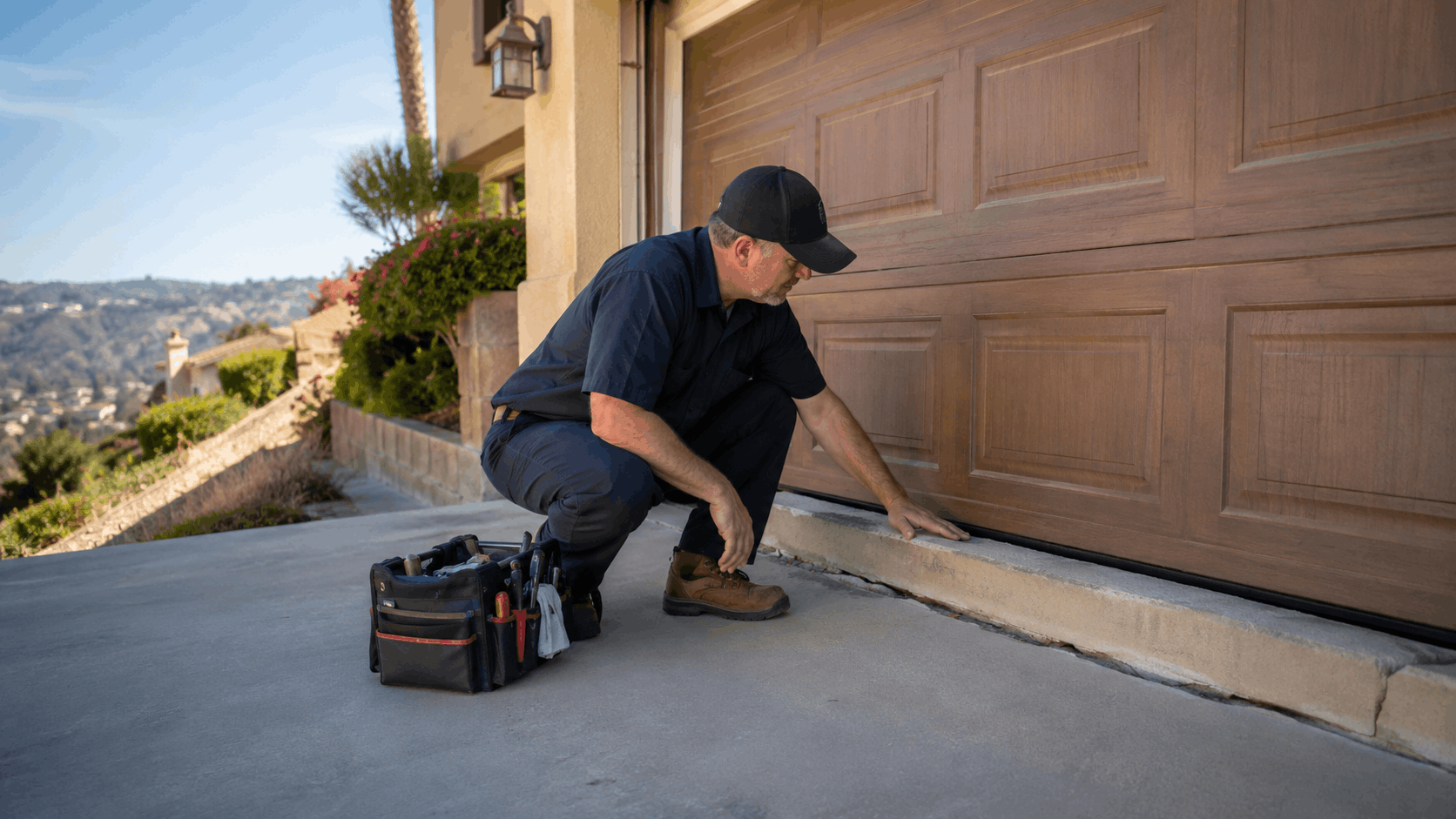 Garage door technician inspecting bottom seal on settled concrete driveway in Irvine