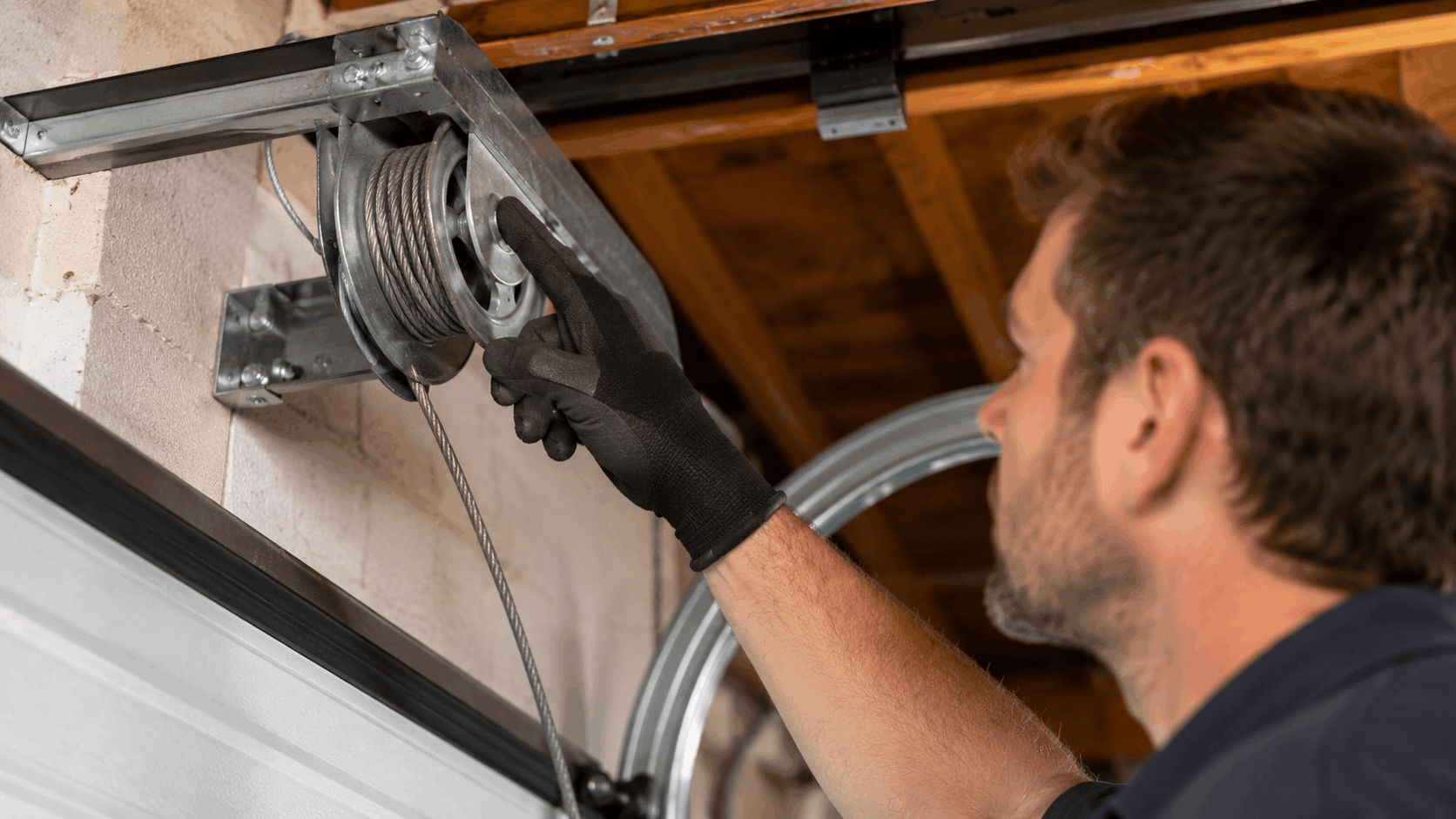 Technician in gloves repairing garage door cable drum and pulley system