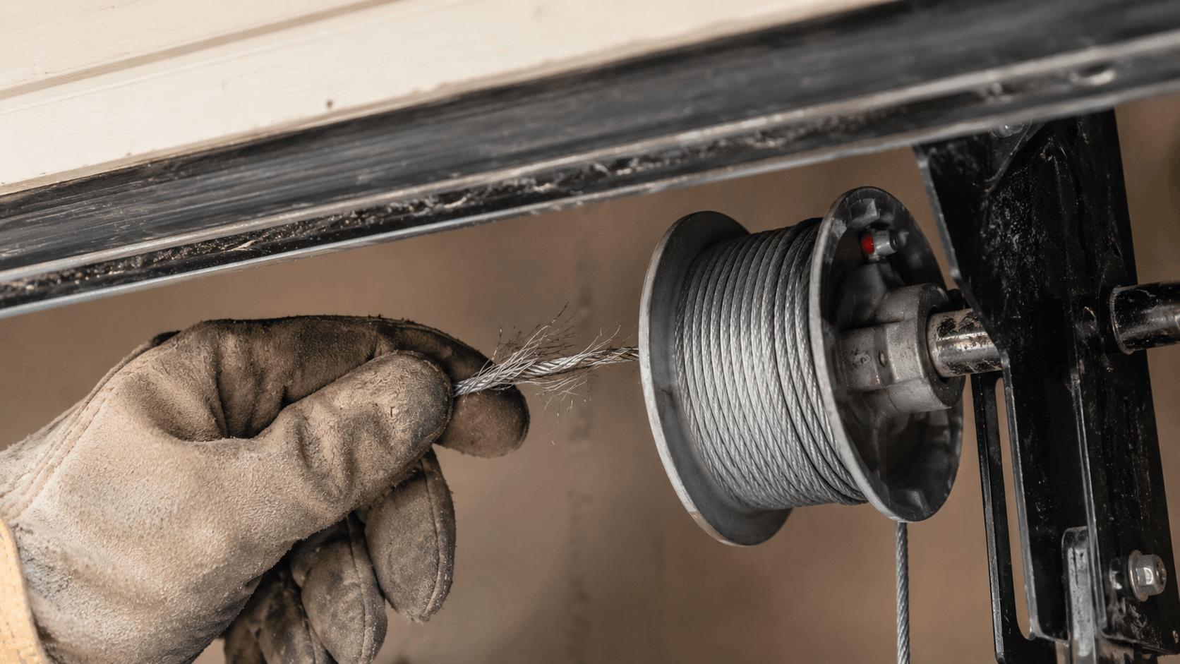 Gloved technician inspecting frayed garage door cable on drum pulley system
