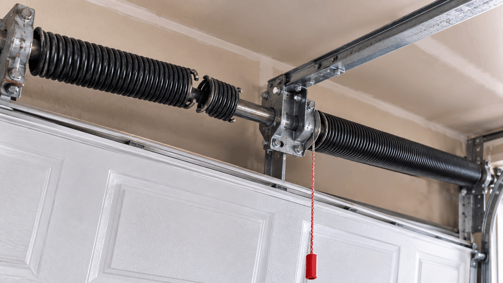 Broken garage door torsion springs above white panel door in Irvine home