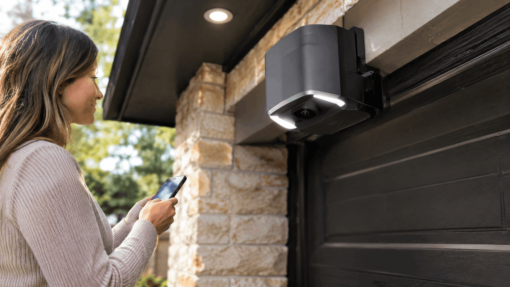 Woman using smartphone app to control garage door security camera with floodlight