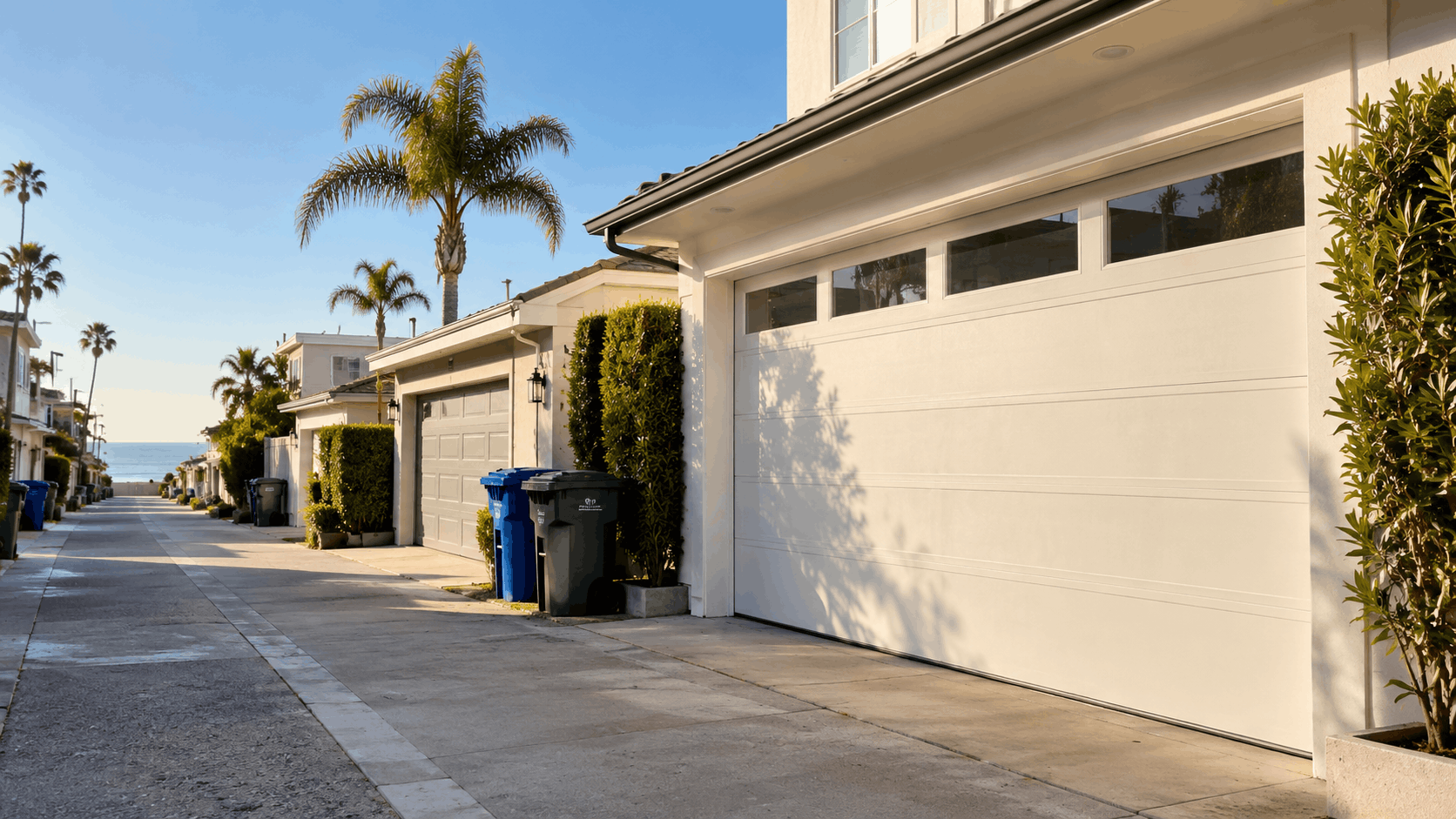 Alley-facing garage doors on Corona del Mar homes with palm trees and ocean view