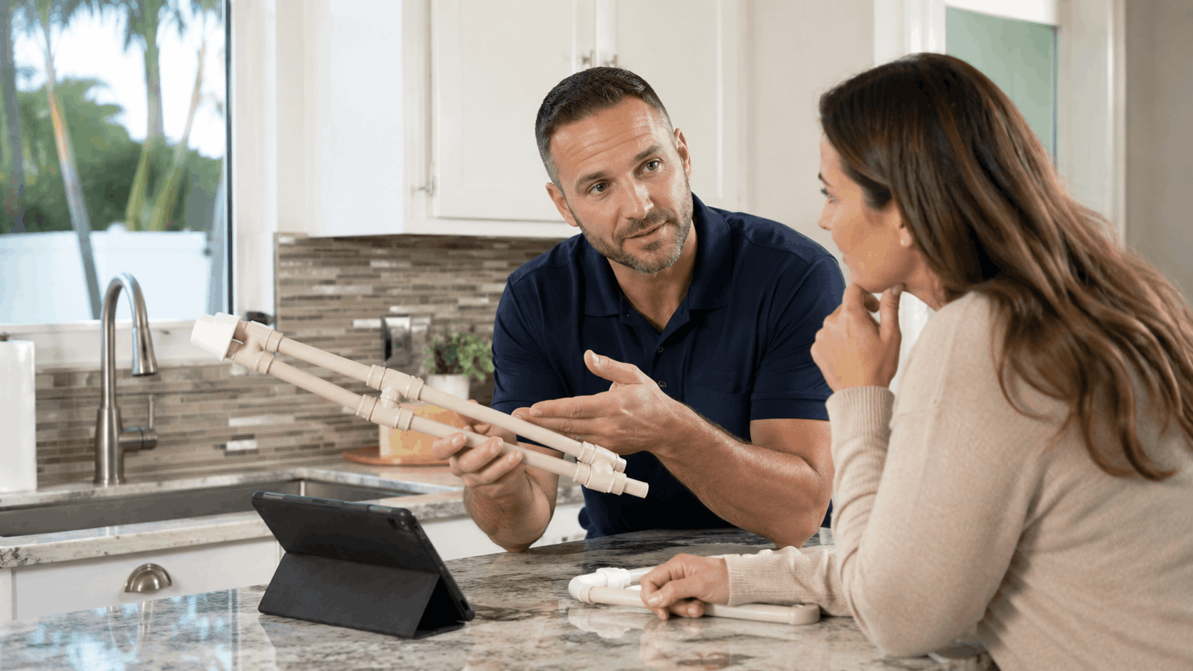 Las Vegas plumber explaining PVC pipe fittings to homeowner at kitchen counter