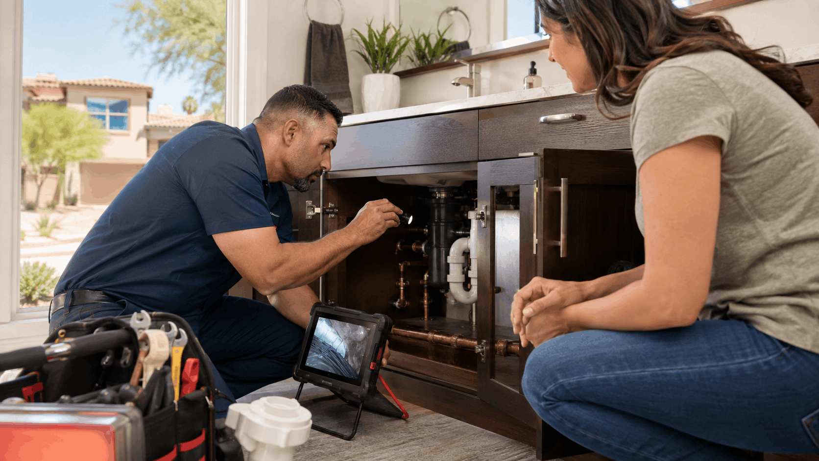 Plumber inspecting under-sink pipes with flashlight and diagnostic tablet in Las Vegas home