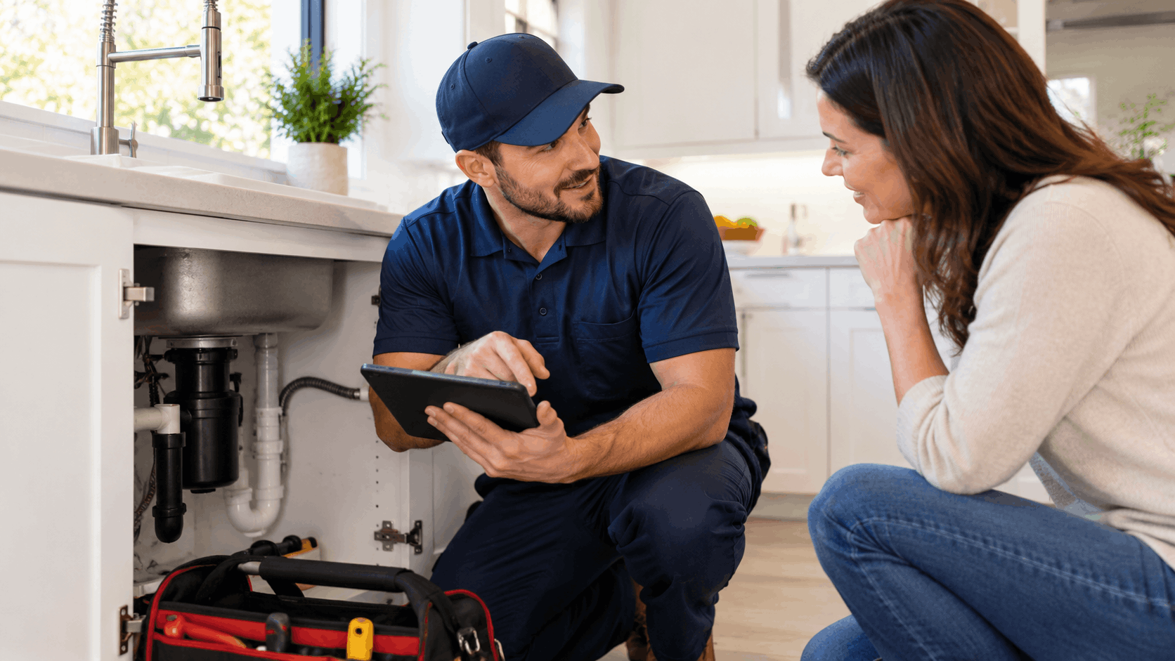 Plumber showing tablet to homeowner while inspecting kitchen sink plumbing in Las Vegas